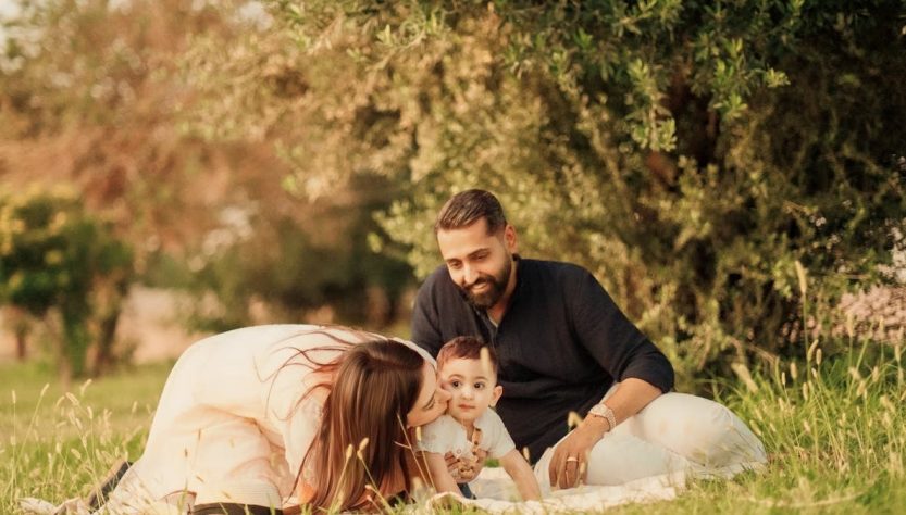 A joyful family with parents and a baby enjoying a sunny day outdoors on a picnic.