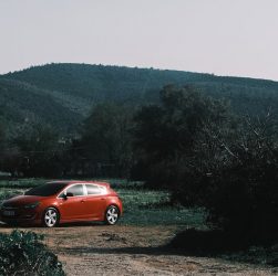 A vibrant red car parked amidst lush green hills and trees under a clear sky.